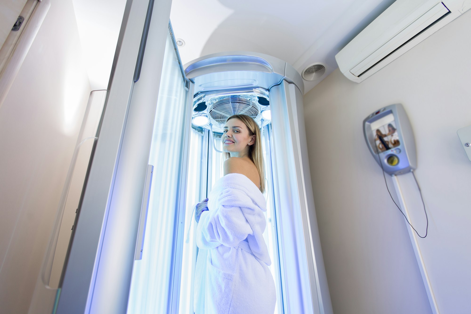 Sexy girl in a white robe is preparing for the tanning procedure in the Solarium. Vertical Solarium